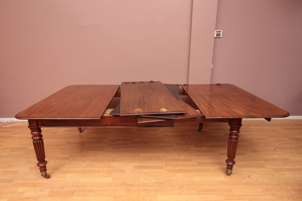 A extended Cuban mahogany dining table featuring additional insert leaves, a polished rectangular top, and four reeded turned legs on brass castors. View X
