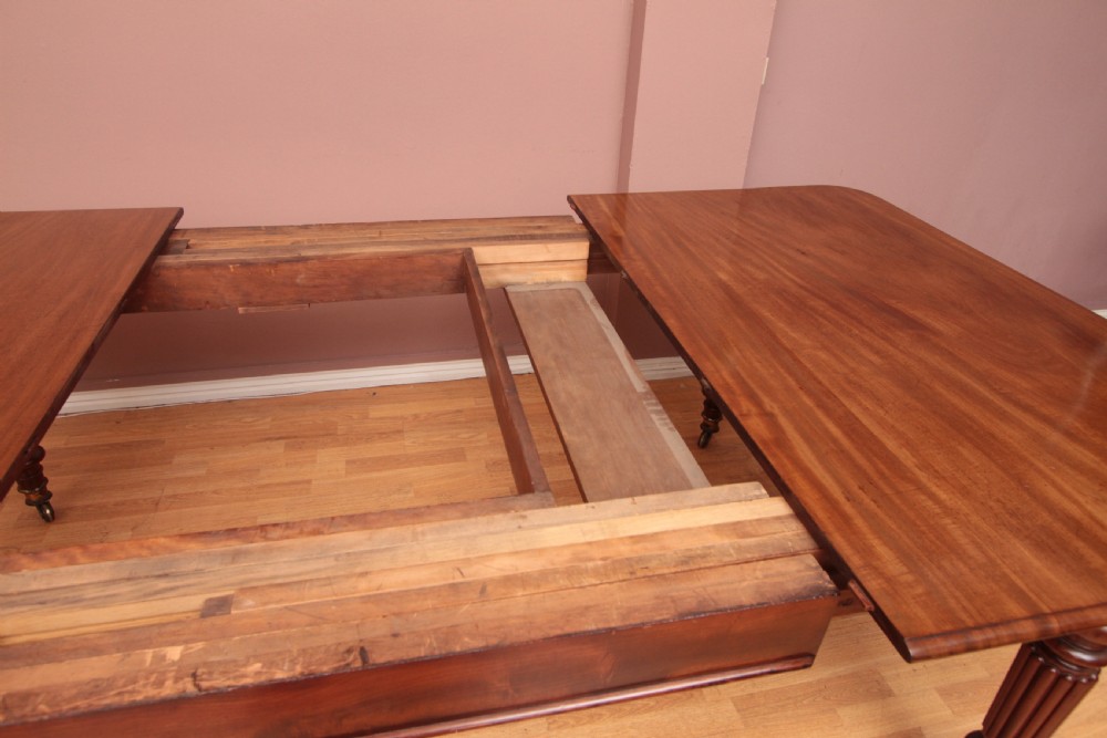 A extended Cuban mahogany dining table featuring additional insert leaves, a polished rectangular top, and four reeded turned legs on brass castors. View XI