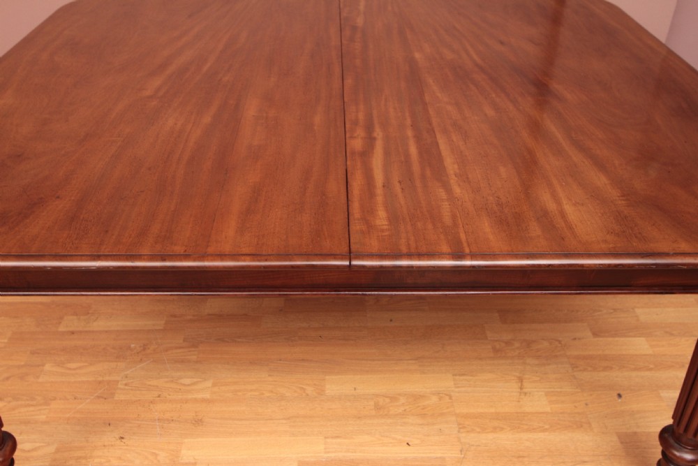 A extended Cuban mahogany dining table featuring additional insert leaves, a polished rectangular top, and four reeded turned legs on brass castors. View XII