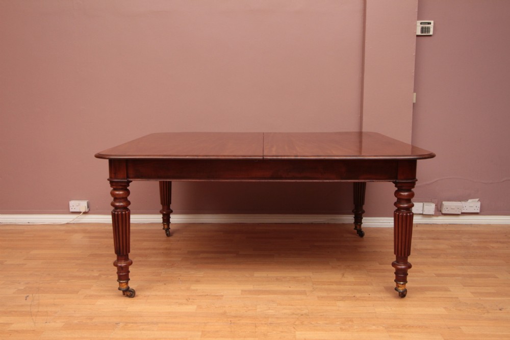 A extended Cuban mahogany dining table featuring additional insert leaves, a polished rectangular top, and four reeded turned legs on brass castors. View XIII