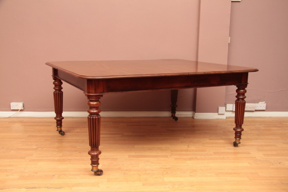 A extended Cuban mahogany dining table featuring additional insert leaves, a polished rectangular top, and four reeded turned legs on brass castors. View XV