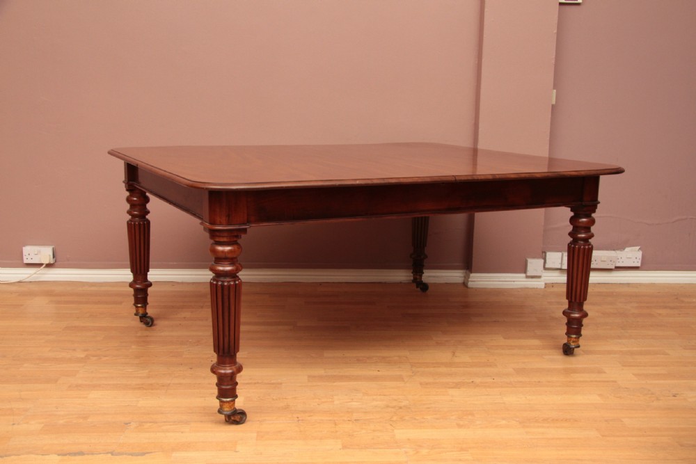 A extended Cuban mahogany dining table featuring additional insert leaves, a polished rectangular top, and four reeded turned legs on brass castors. View XVI