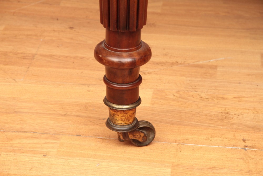 A extended Cuban mahogany dining table featuring additional insert leaves, a polished rectangular top, and four reeded turned legs on brass castors. View XVII