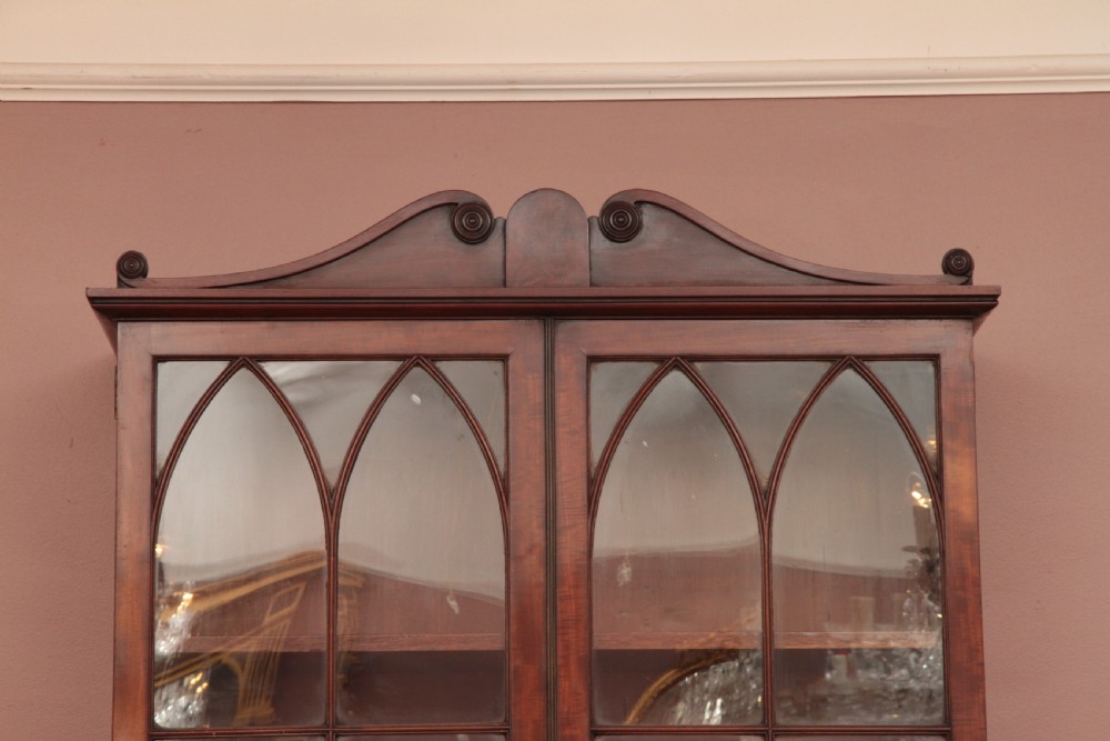 An antique dark mahogany bureau bookcase featuring a shaped pediment, twin astragal glazed doors, and four lower drawers with oval brass handles. View II