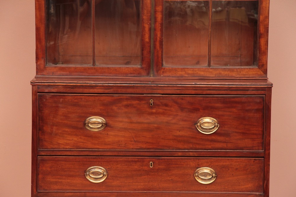 An antique dark mahogany bureau bookcase featuring a shaped pediment, twin astragal glazed doors, and four lower drawers with oval brass handles. View III