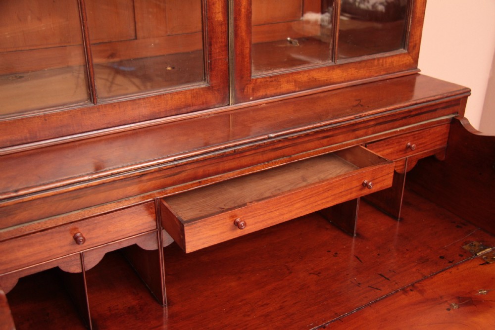 An antique dark mahogany bureau bookcase featuring a shaped pediment, twin astragal glazed doors, and four lower drawers with oval brass handles. View V