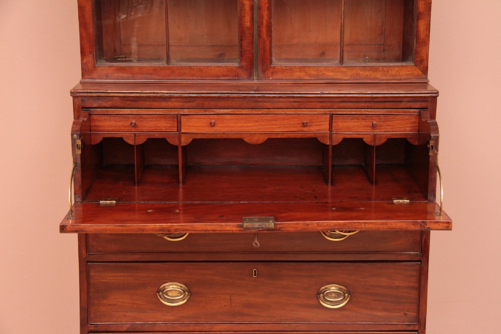 An antique dark mahogany bureau bookcase featuring a shaped pediment, twin astragal glazed doors, and four lower drawers with oval brass handles. View VI
