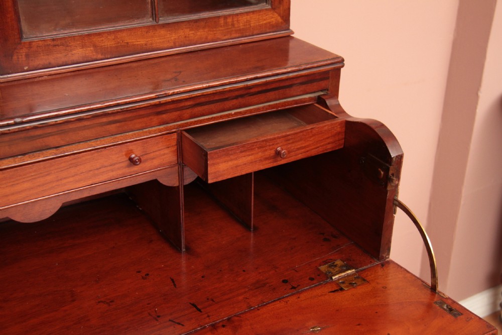An antique dark mahogany bureau bookcase featuring a shaped pediment, twin astragal glazed doors, and four lower drawers with oval brass handles. View VII