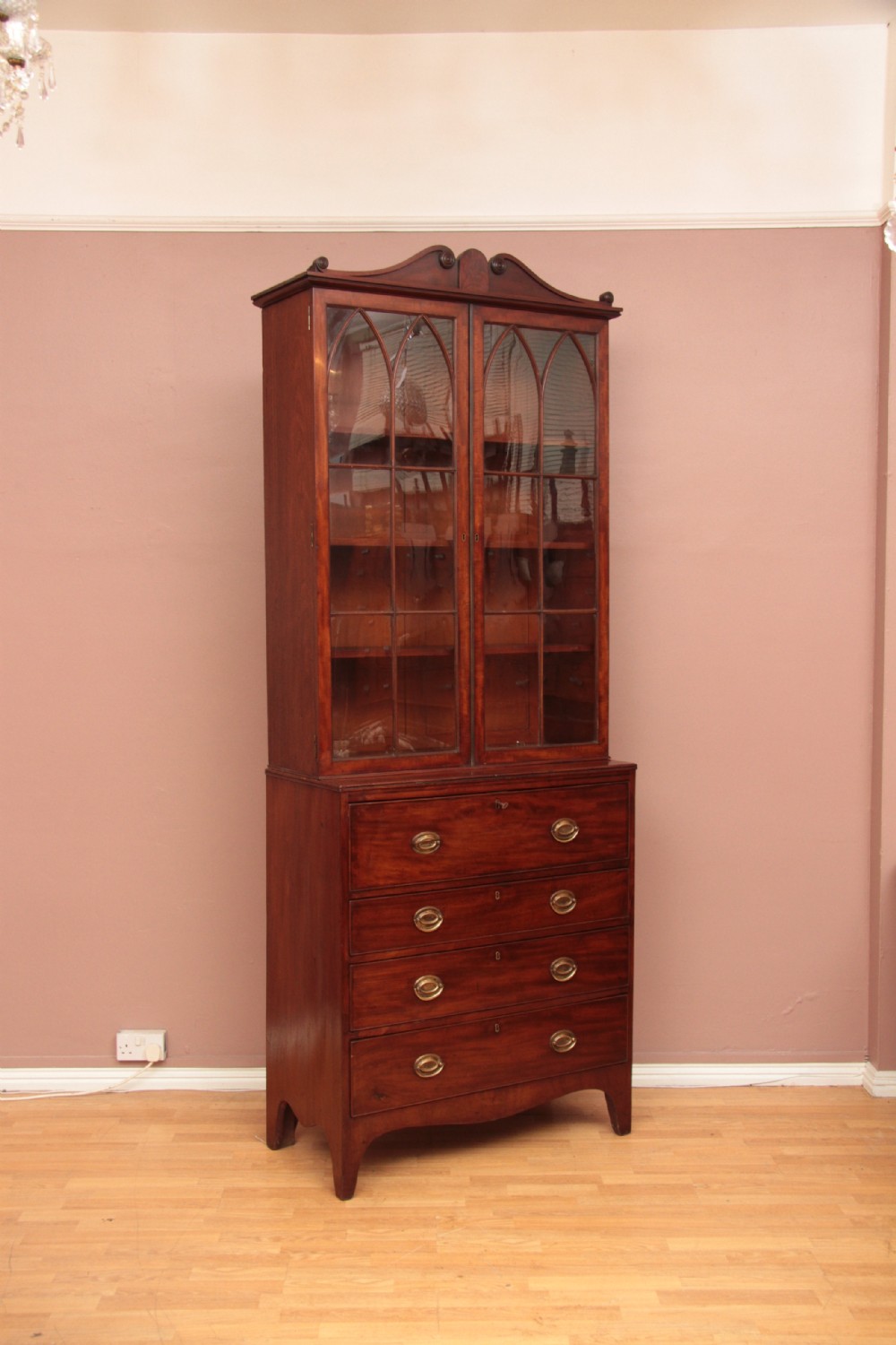 An antique dark mahogany bureau bookcase featuring a shaped pediment, twin astragal glazed doors, and four lower drawers with oval brass handles. View VIII