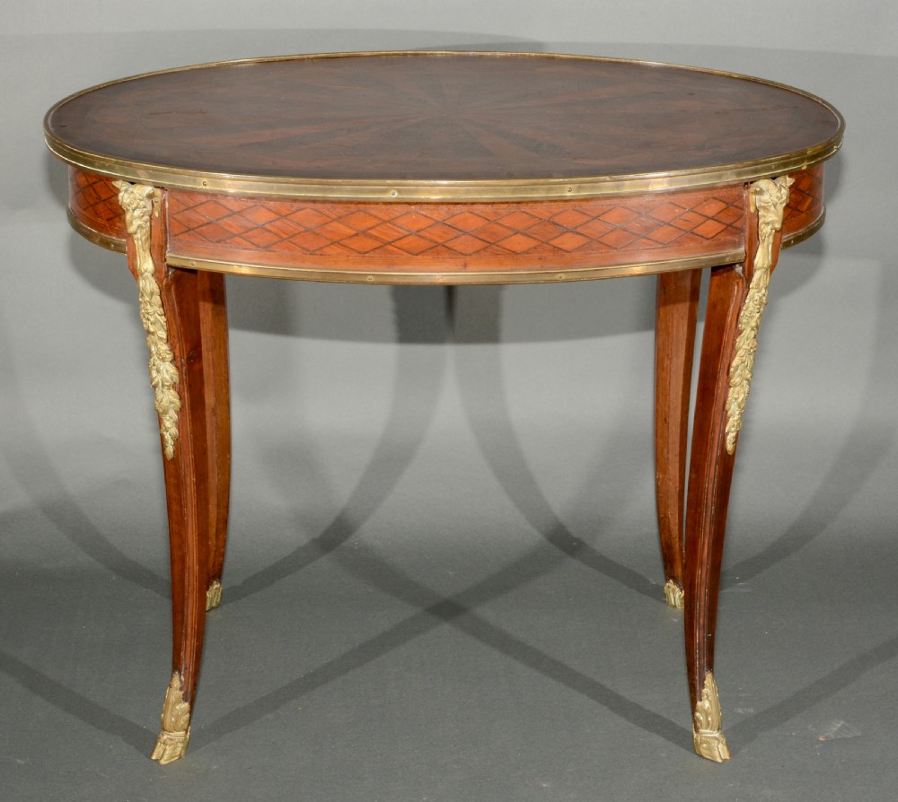 A 19th-century French Louis XV style oval centre table featuring sunburst and diaper marquetry, polished gilt bronze rim and mounts, resting on curved legs ending in hoof feet.
