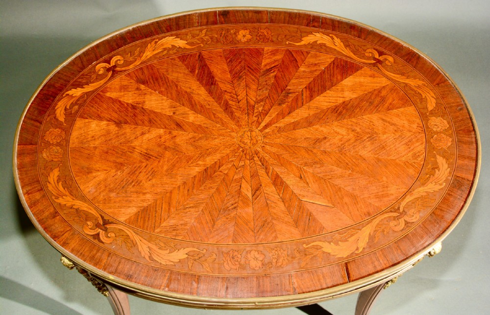 A 19th-century French Louis XV style oval centre table featuring sunburst and diaper marquetry, polished gilt bronze rim and mounts, resting on curved legs ending in hoof feet. View VI