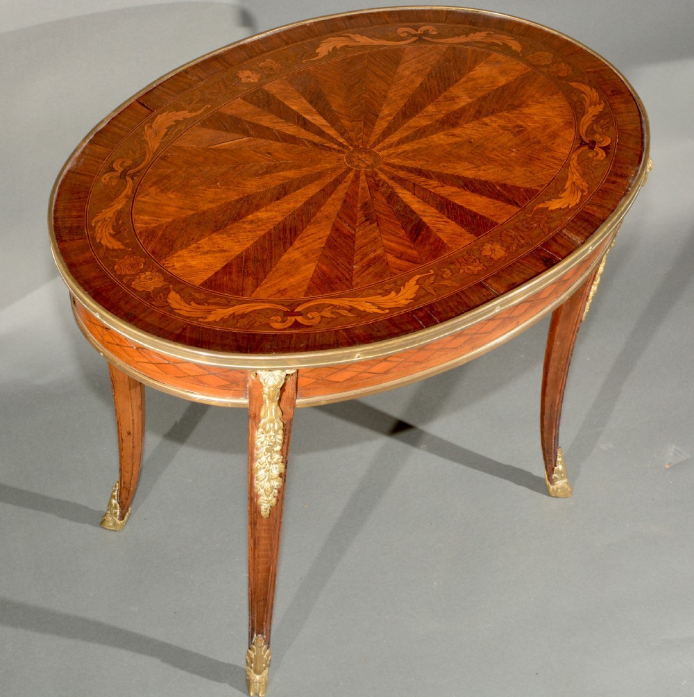 A 19th-century French Louis XV style oval centre table featuring sunburst and diaper marquetry, polished gilt bronze rim and mounts, resting on curved legs ending in hoof feet. View VII