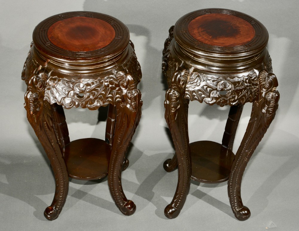 A pair of dark wood carved Asian plant stands featuring round inset tops, openwork aprons, cabriole legs, and lower circular shelves.