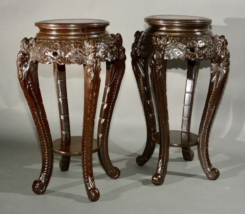 A pair of dark wood carved Asian plant stands featuring round inset tops, openwork aprons, cabriole legs, and lower circular shelves. View V