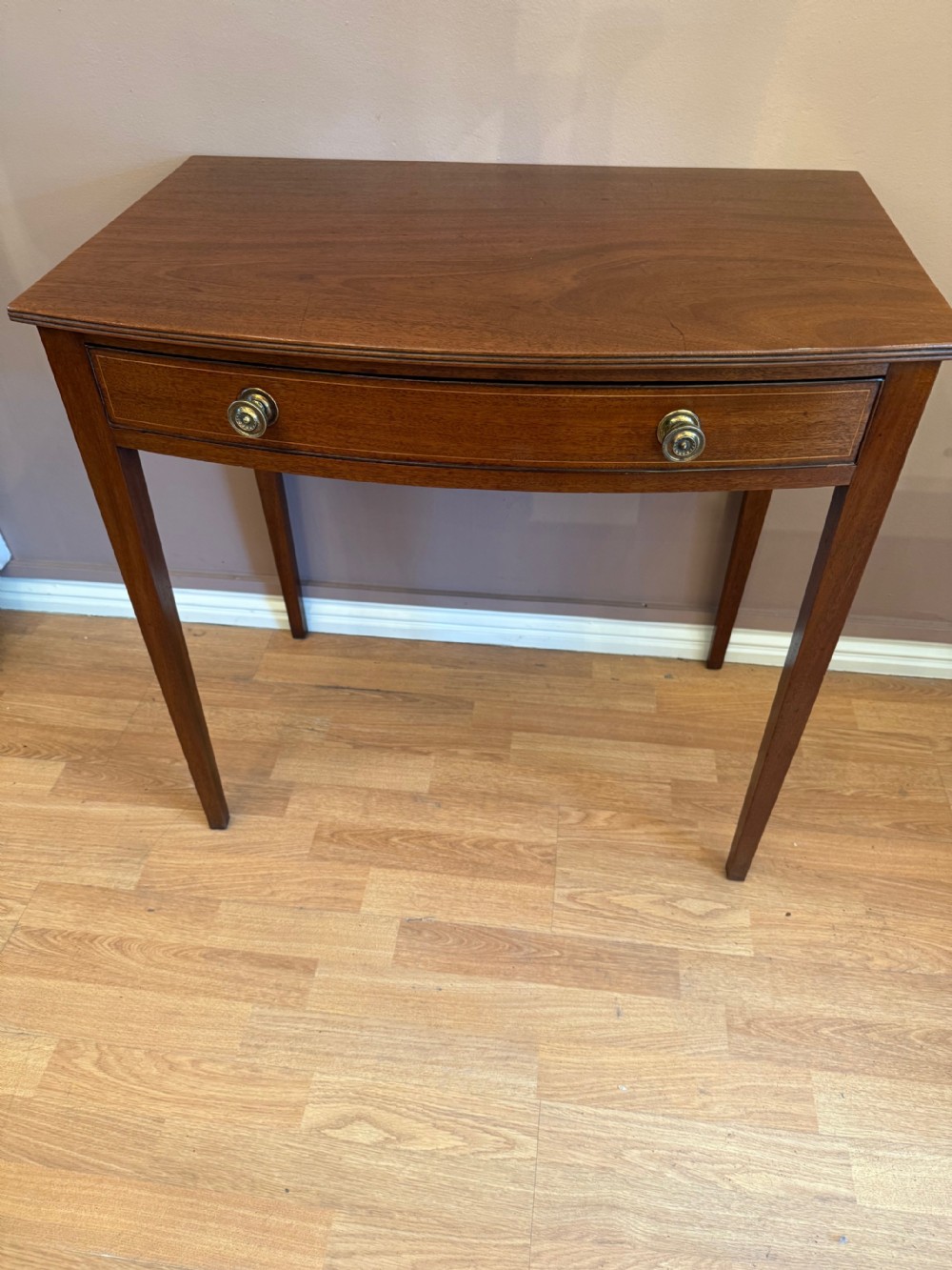 A mahogany bow-fronted side table featuring a single drawer with two circular brass knobs, supported by four tapered square legs. View II