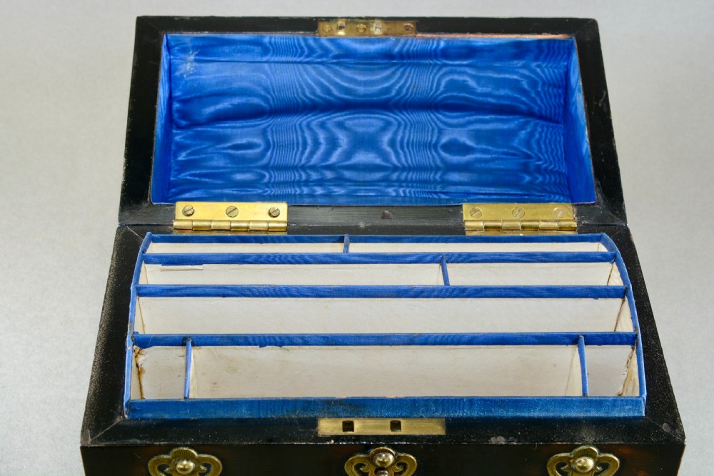 A dark coromandel wood domed stationery box decorated with intricate engraved brass straps and central keyhole. View II
