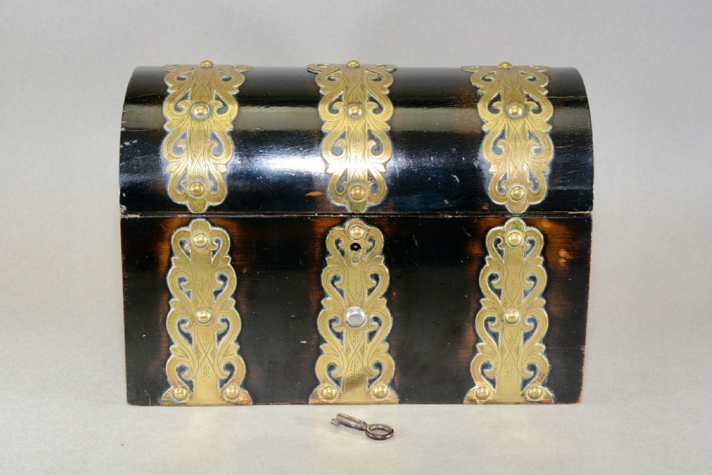 A dark coromandel wood domed stationery box decorated with intricate engraved brass straps and central keyhole.