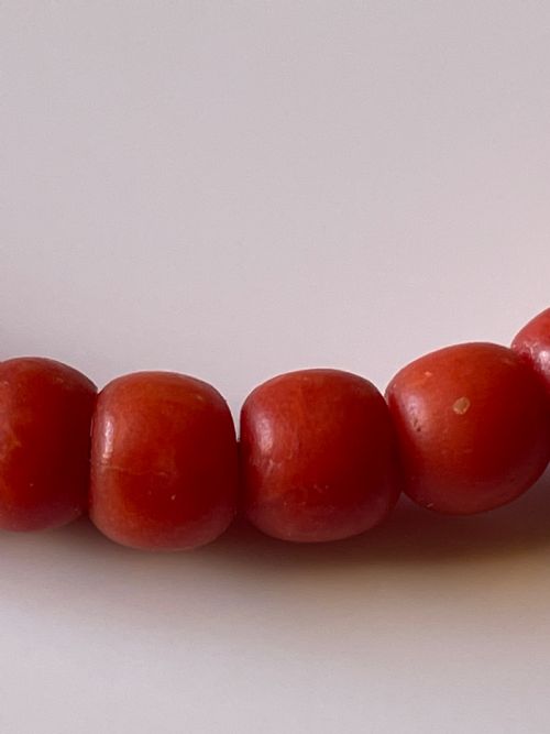 fig 2. A hand holding a single strand of natural un-dyed red coral beads featuring a gold push clasp.
