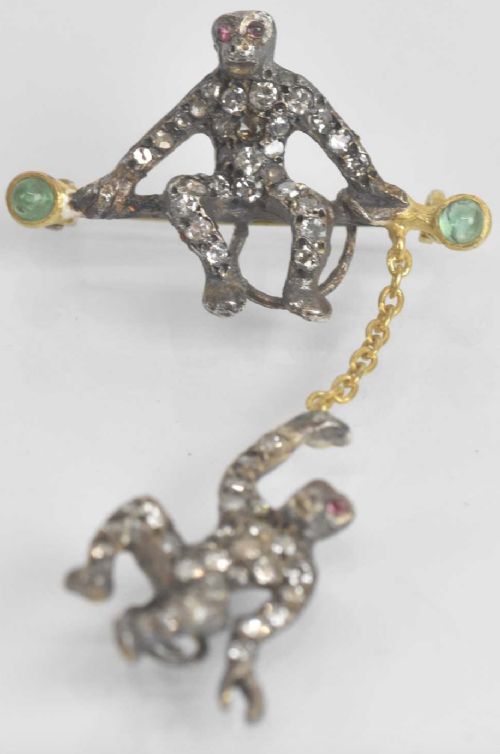 fig 1. Victorian bar brooch featuring two pave diamond-set monkeys, one perched on a gold bar with green emerald terminals and one dangling below from a chain.