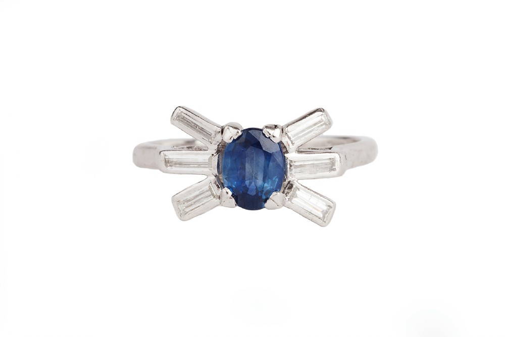 An Art Deco platinum ring featuring a central oval blue sapphire flanked by fanned baguette-cut diamonds.