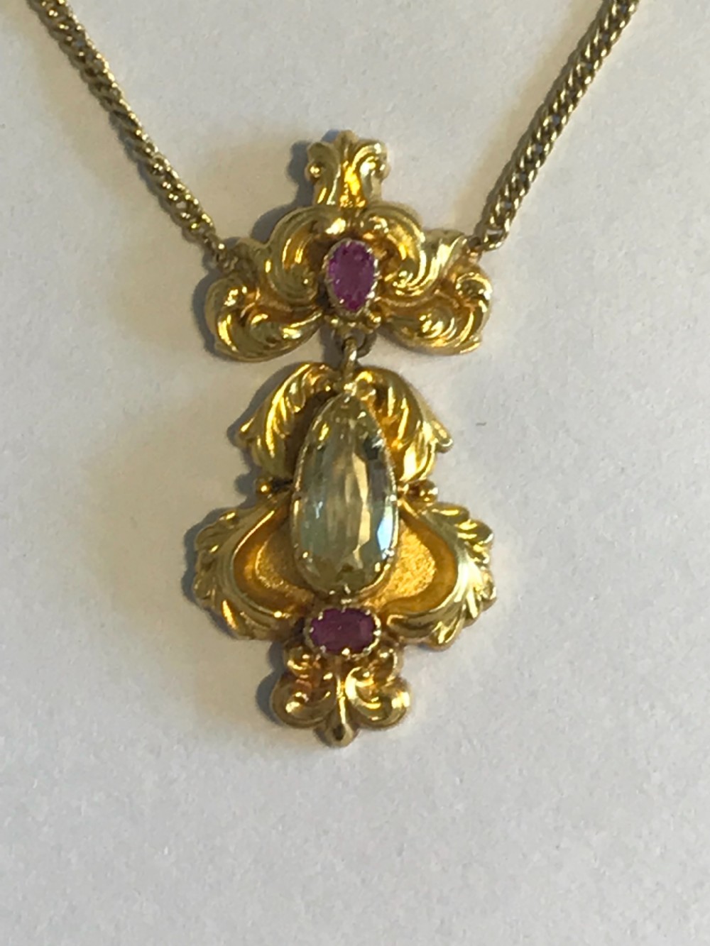 An ornate 9ct yellow gold scrollwork pendant set with a central teardrop-cut citrine and two pink rubies, suspended from a gold chain. View III
