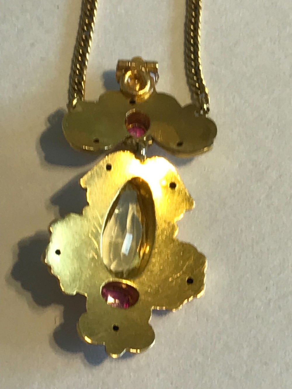 An ornate 9ct yellow gold scrollwork pendant set with a central teardrop-cut citrine and two pink rubies, suspended from a gold chain. View IV