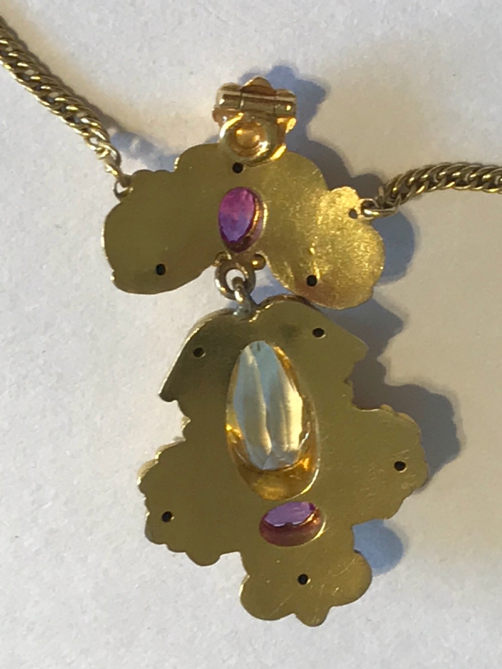 An ornate 9ct yellow gold scrollwork pendant set with a central teardrop-cut citrine and two pink rubies, suspended from a gold chain. View V