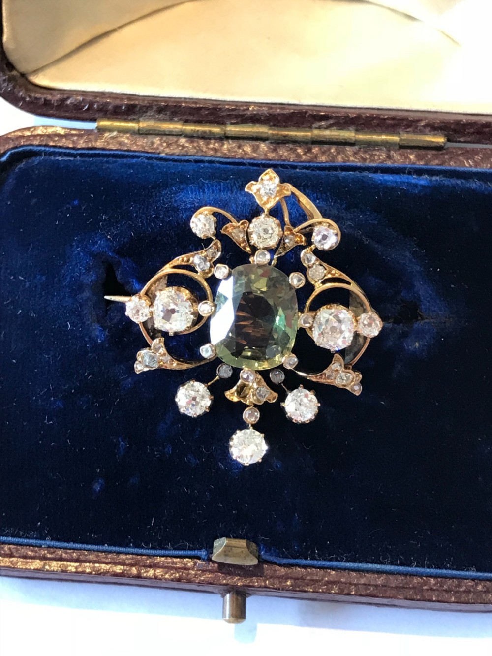 A Victorian gold pendant featuring a central cushion-cut green sapphire within an openwork diamond-set scrollwork frame.
