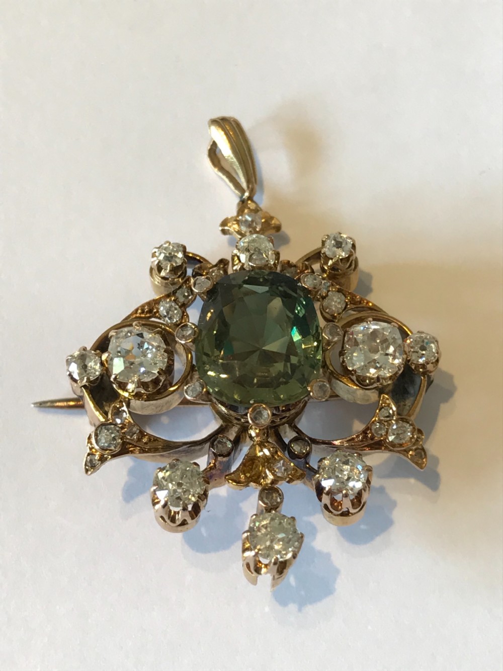 A Victorian gold pendant featuring a central cushion-cut green sapphire within an openwork diamond-set scrollwork frame. View IV