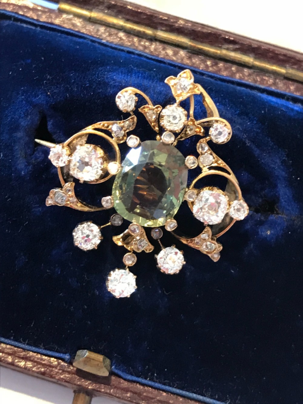 A Victorian gold pendant featuring a central cushion-cut green sapphire within an openwork diamond-set scrollwork frame. View VII