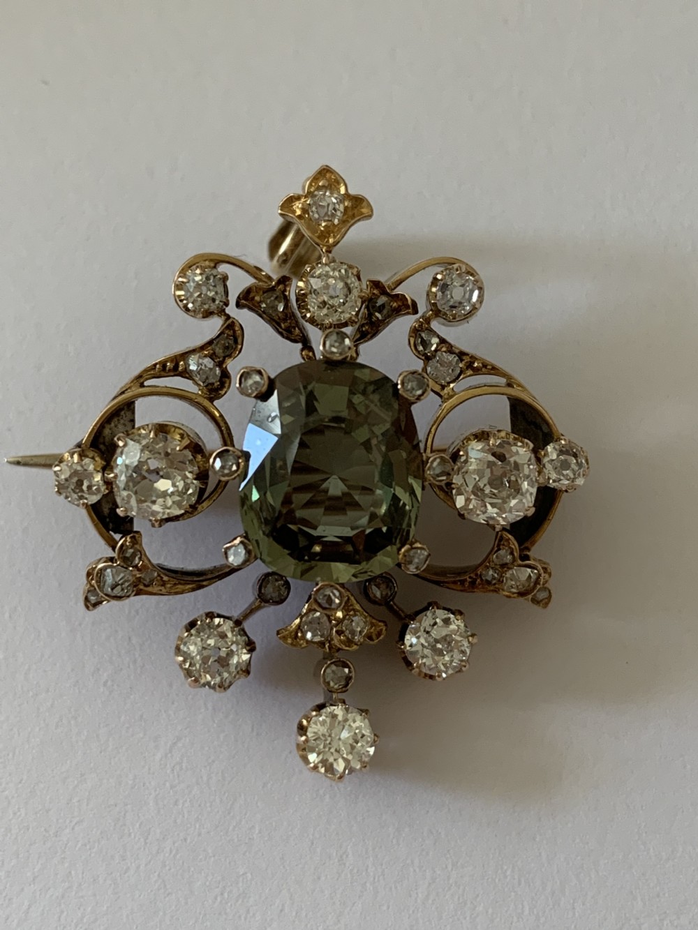 A Victorian gold pendant featuring a central cushion-cut green sapphire within an openwork diamond-set scrollwork frame. View II