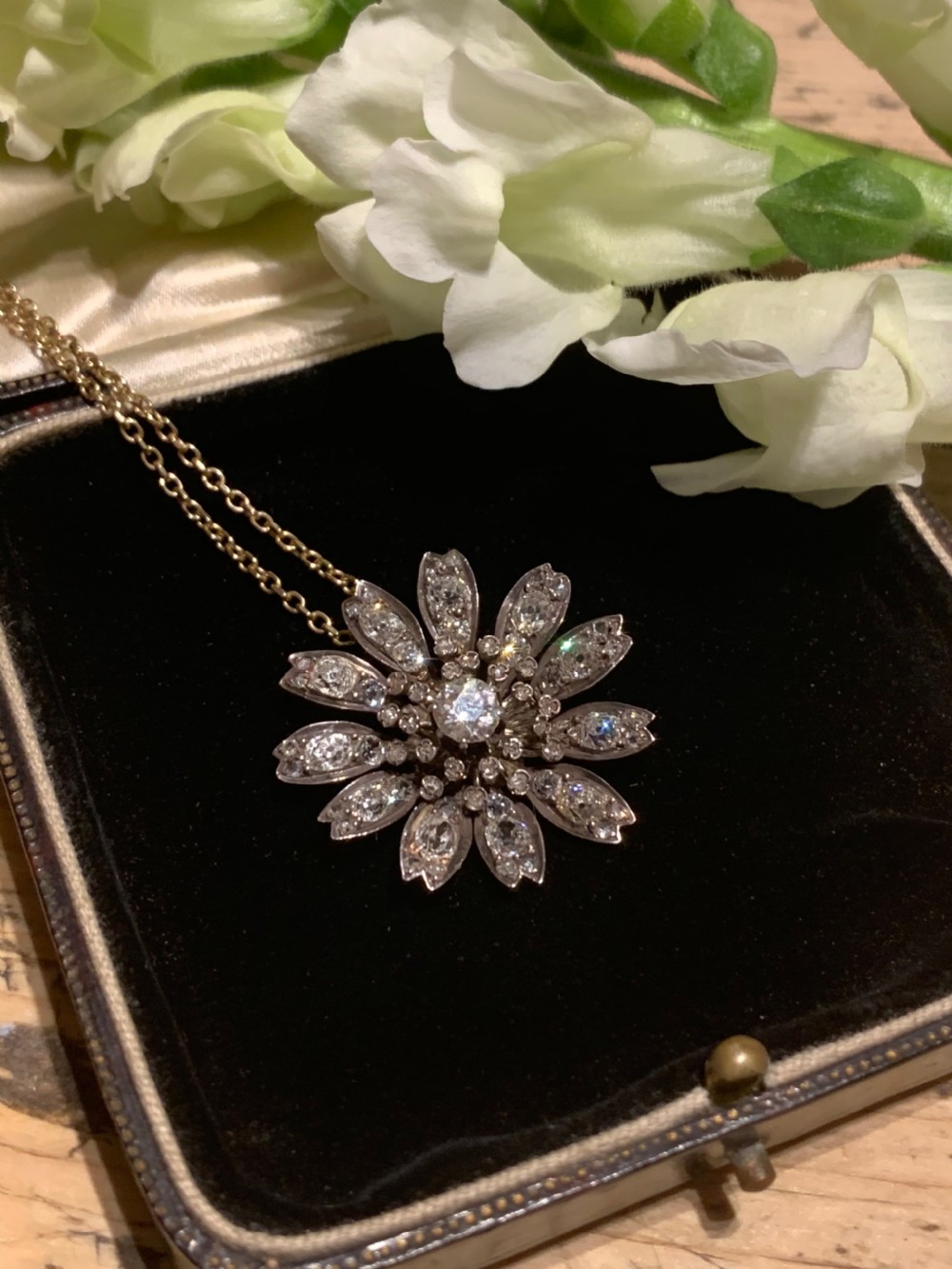 A Victorian diamond flower-shaped pendant featuring old cut and rose cut diamonds set in silver and gold suspended on a fine chain.