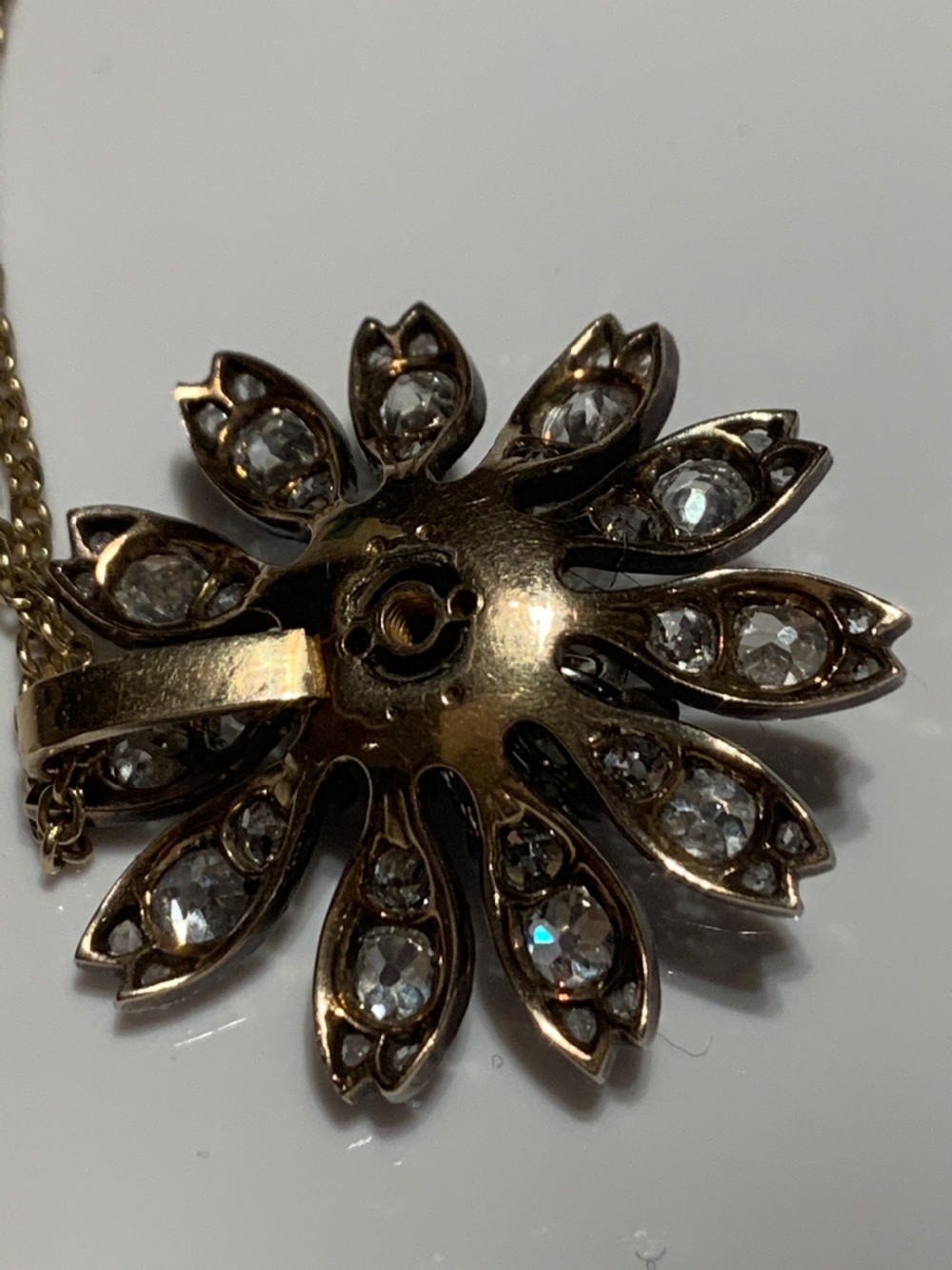 A Victorian diamond flower-shaped pendant featuring old cut and rose cut diamonds set in silver and gold suspended on a fine chain. View III