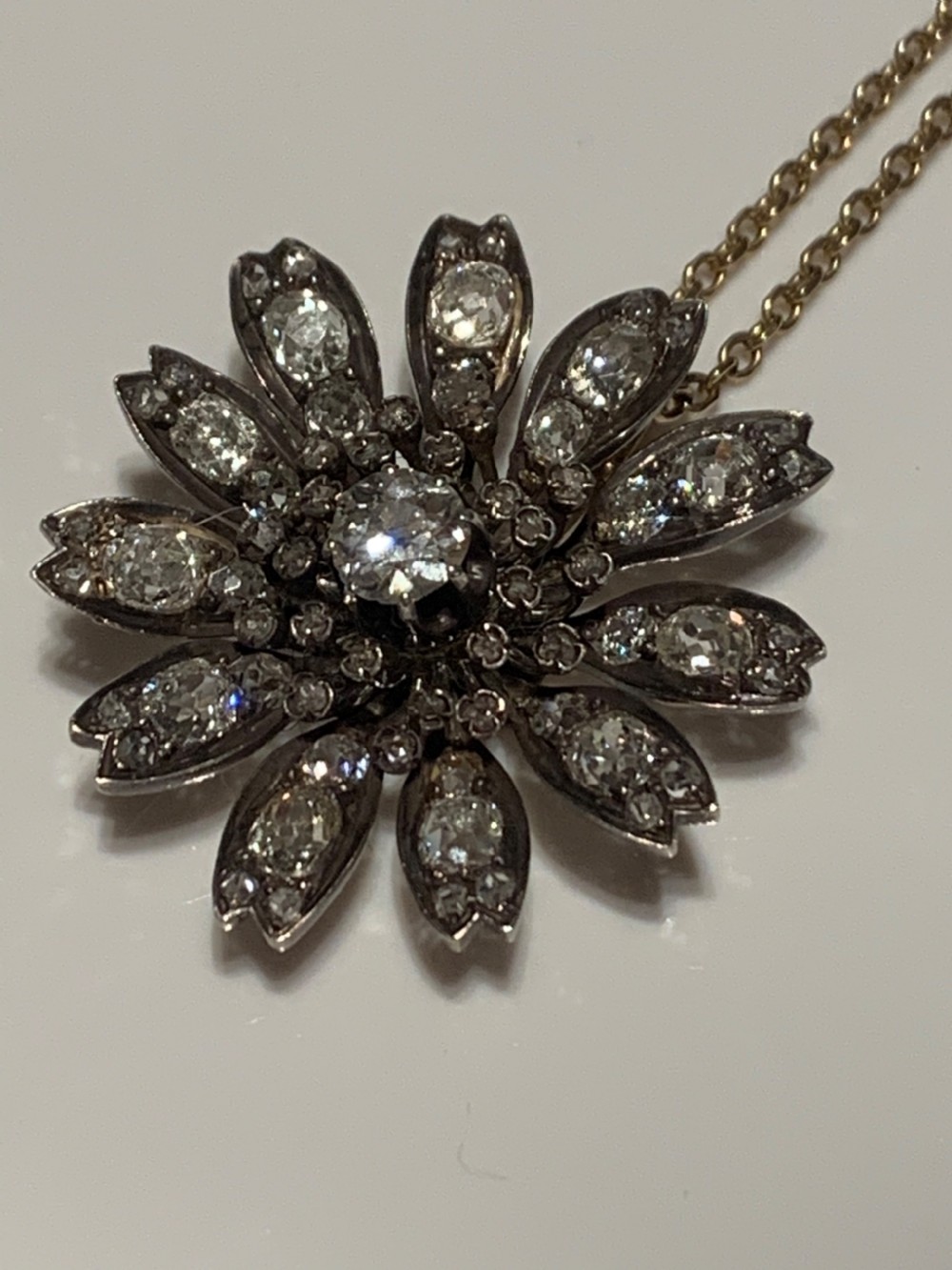 A Victorian diamond flower-shaped pendant featuring old cut and rose cut diamonds set in silver and gold suspended on a fine chain. View IV