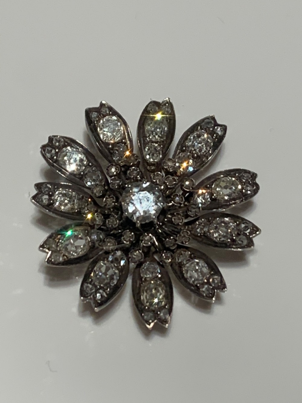 A Victorian diamond flower-shaped pendant featuring old cut and rose cut diamonds set in silver and gold suspended on a fine chain. View V