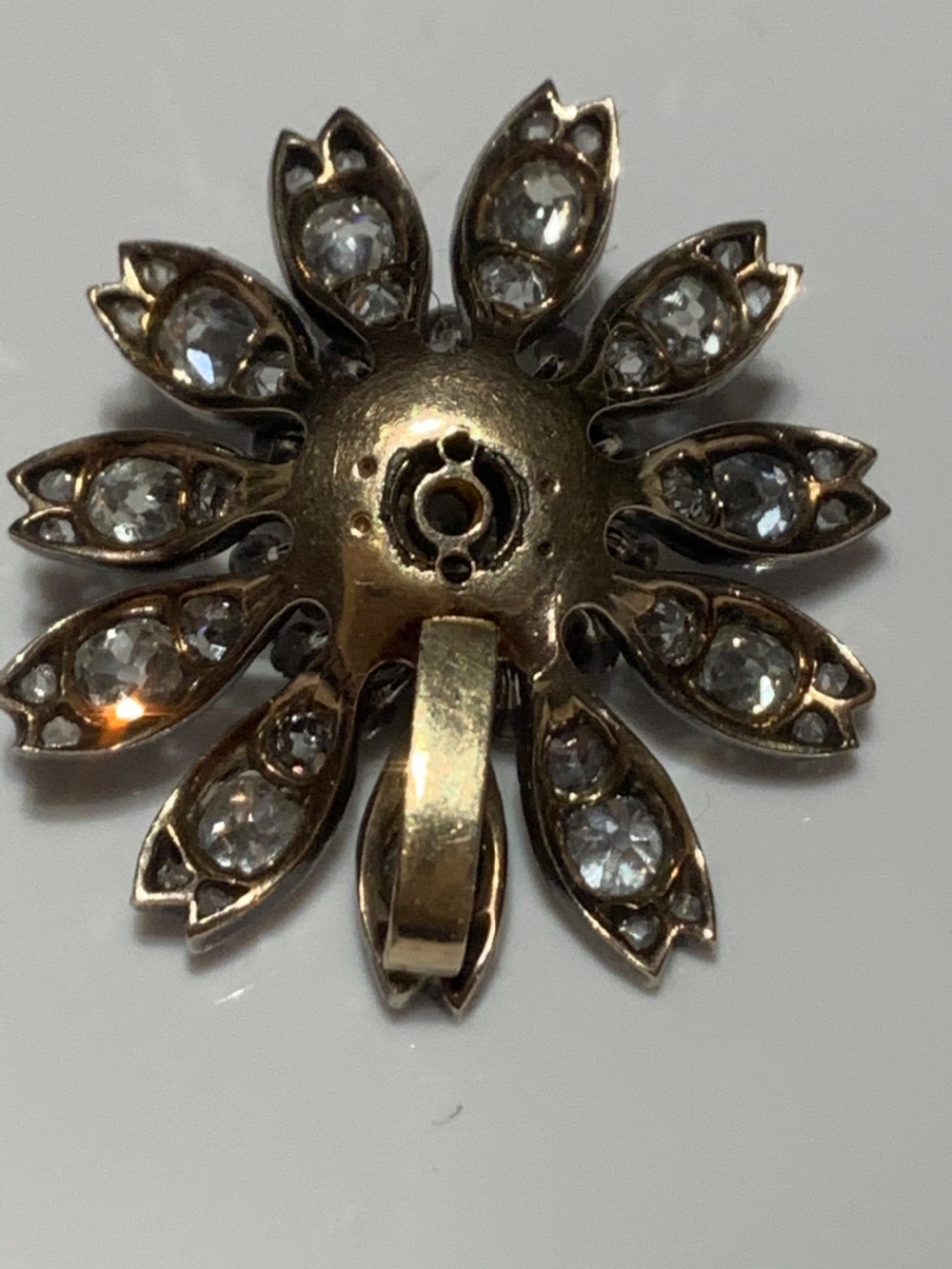A Victorian diamond flower-shaped pendant featuring old cut and rose cut diamonds set in silver and gold suspended on a fine chain. View VI