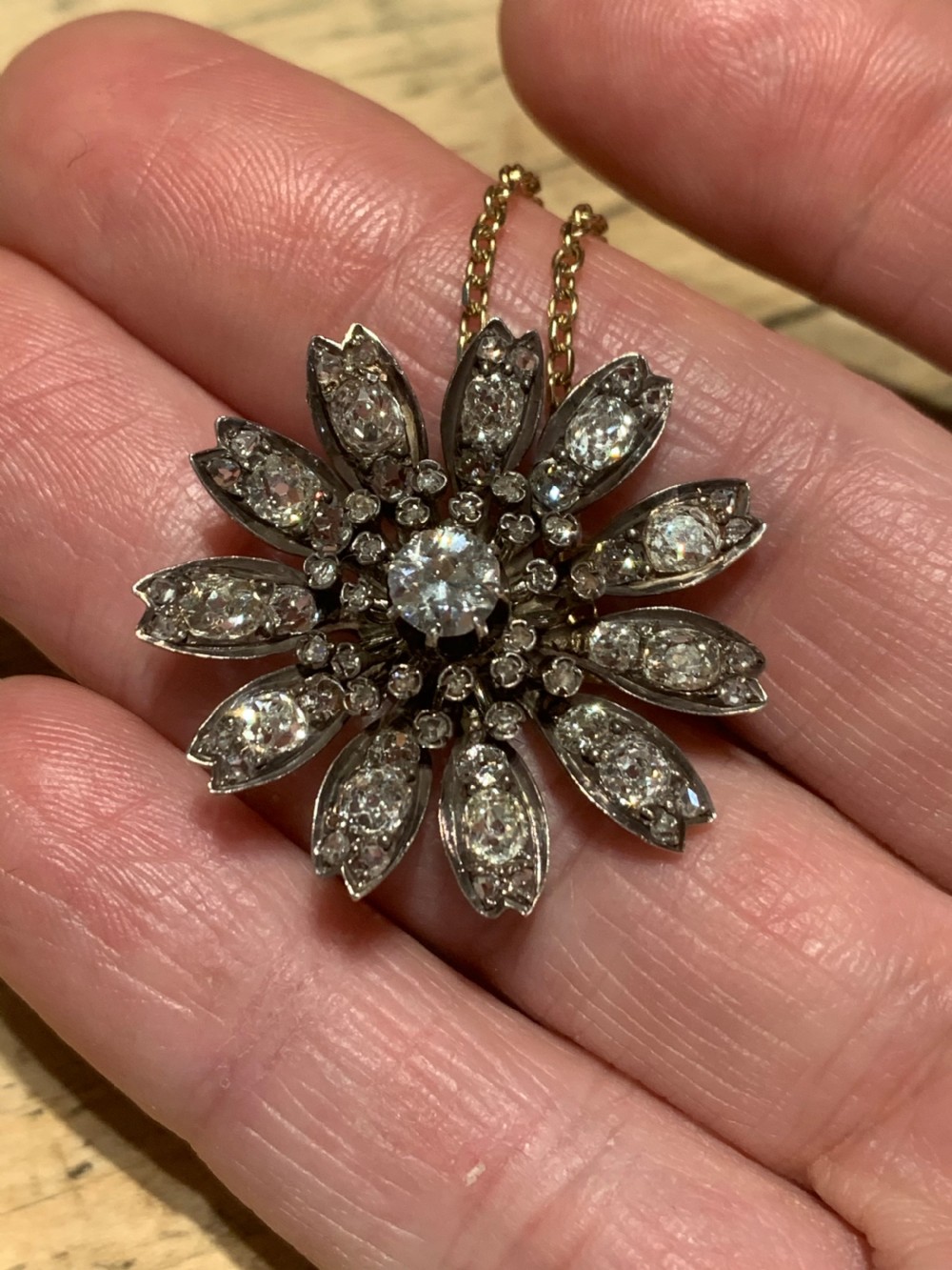 A Victorian diamond flower-shaped pendant featuring old cut and rose cut diamonds set in silver and gold suspended on a fine chain. View VIII
