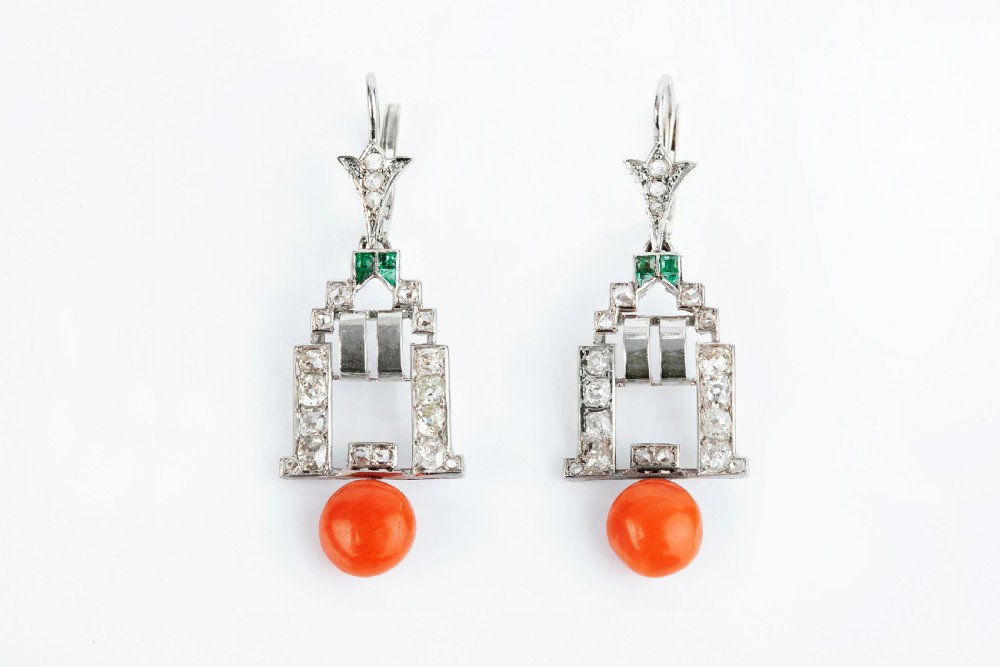 A pair of Art Deco drop earrings in white metal featuring geometric diamond settings, square emerald accents, and spherical orange coral drops.
