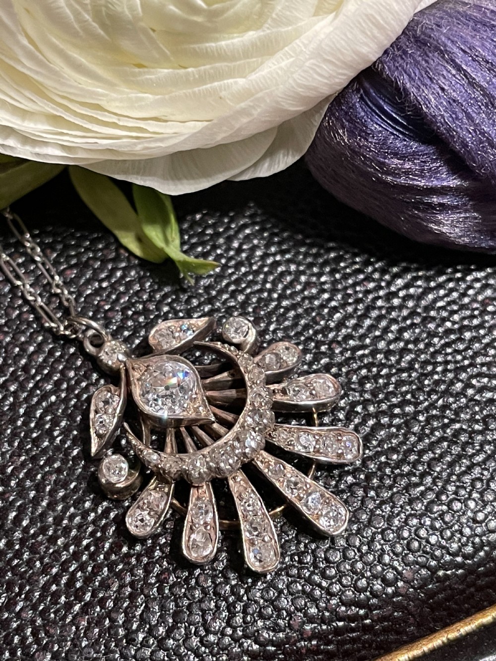 An Edwardian platinum pendant featuring an openwork sunburst design encrusted with diamonds around a central stone.