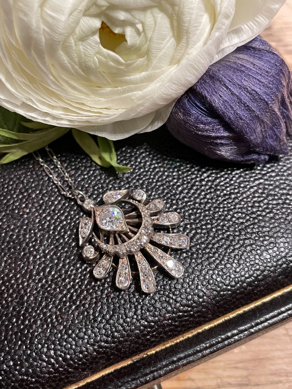 An Edwardian platinum pendant featuring an openwork sunburst design encrusted with diamonds around a central stone. View II