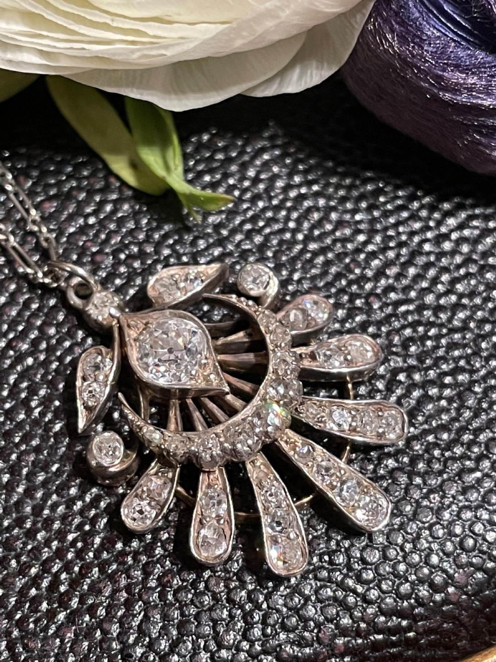 An Edwardian platinum pendant featuring an openwork sunburst design encrusted with diamonds around a central stone. View III