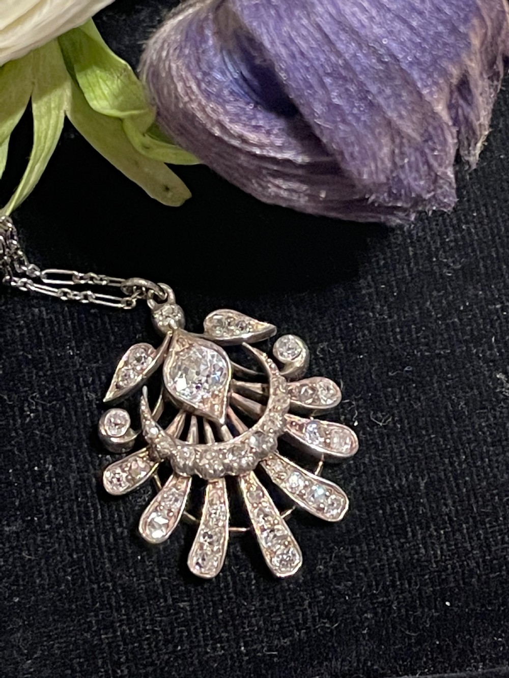 An Edwardian platinum pendant featuring an openwork sunburst design encrusted with diamonds around a central stone. View IV