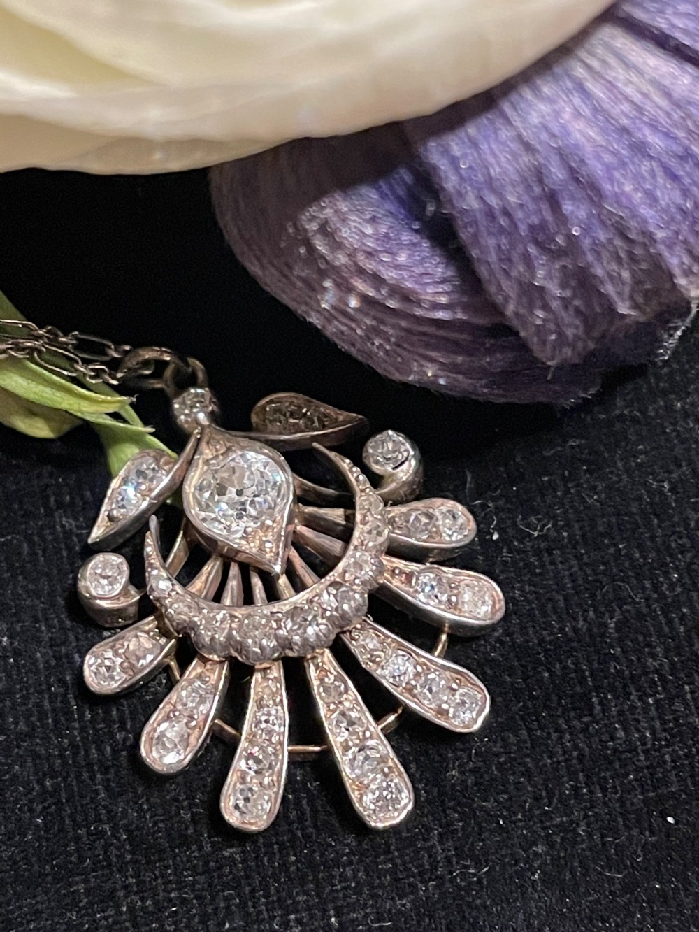 An Edwardian platinum pendant featuring an openwork sunburst design encrusted with diamonds around a central stone. View V