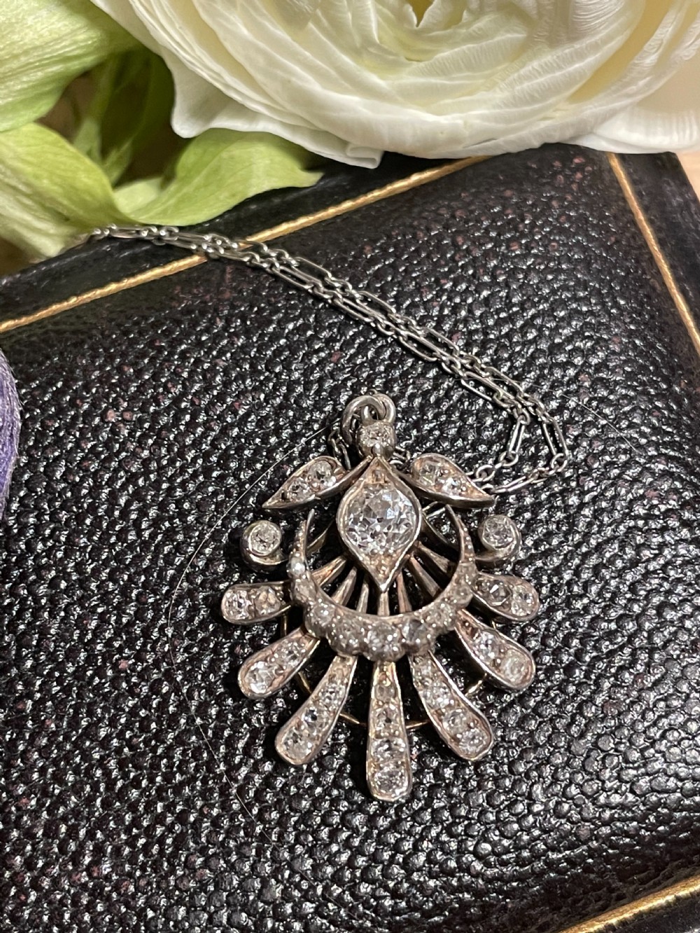 An Edwardian platinum pendant featuring an openwork sunburst design encrusted with diamonds around a central stone. View VI