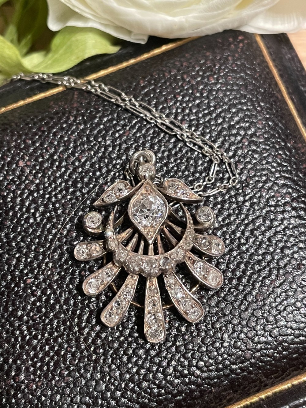 An Edwardian platinum pendant featuring an openwork sunburst design encrusted with diamonds around a central stone. View VII