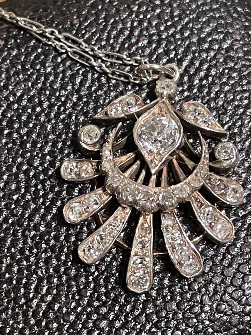 An Edwardian platinum pendant featuring an openwork sunburst design encrusted with diamonds around a central stone. View VIII