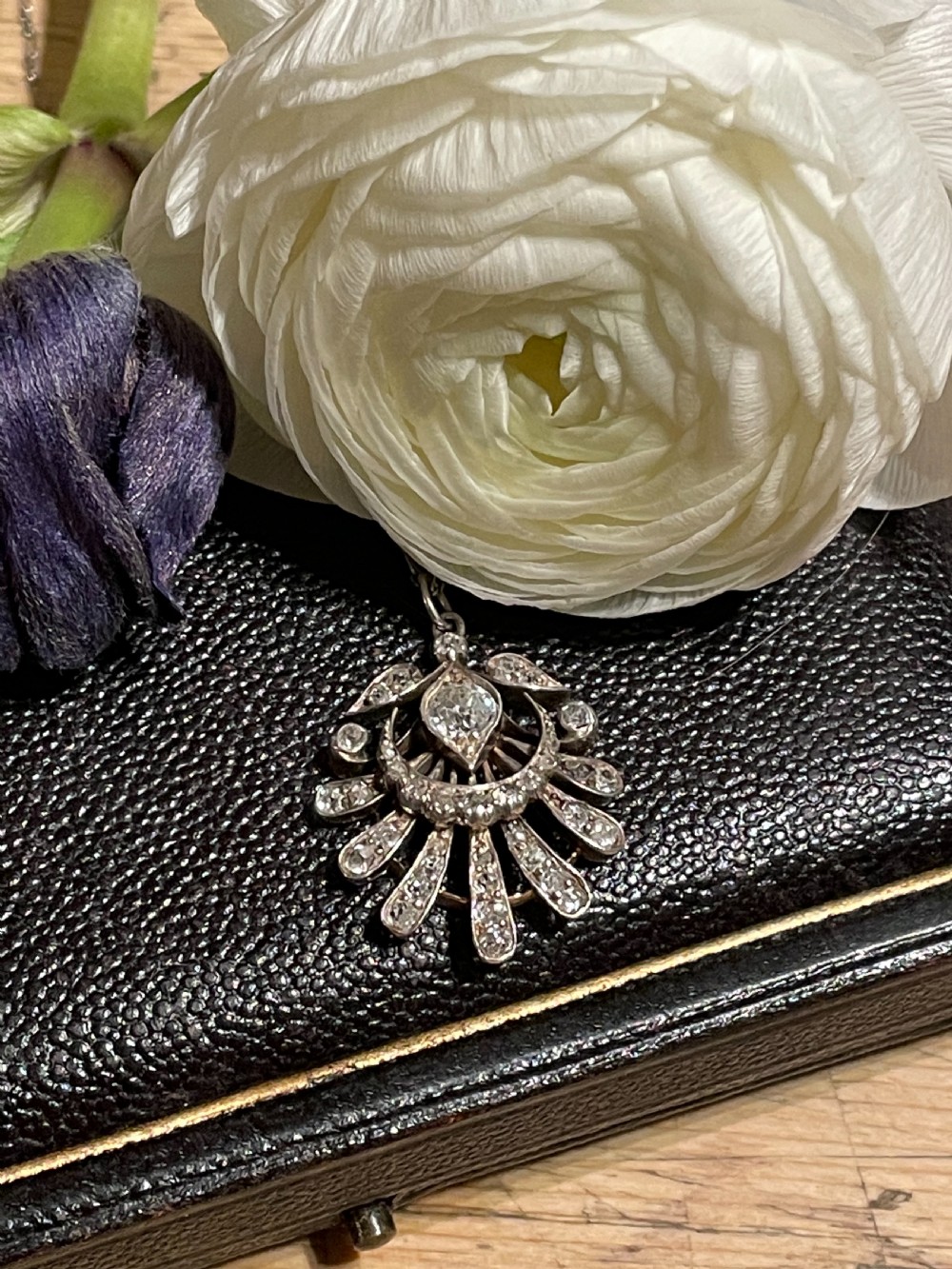 An Edwardian platinum pendant featuring an openwork sunburst design encrusted with diamonds around a central stone. View IX