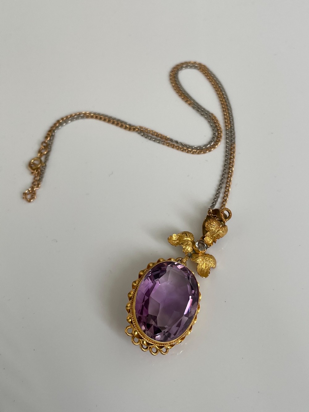 An oval purple faceted amethyst pendant with an ornate foliate gold bail on a delicate chain. View II