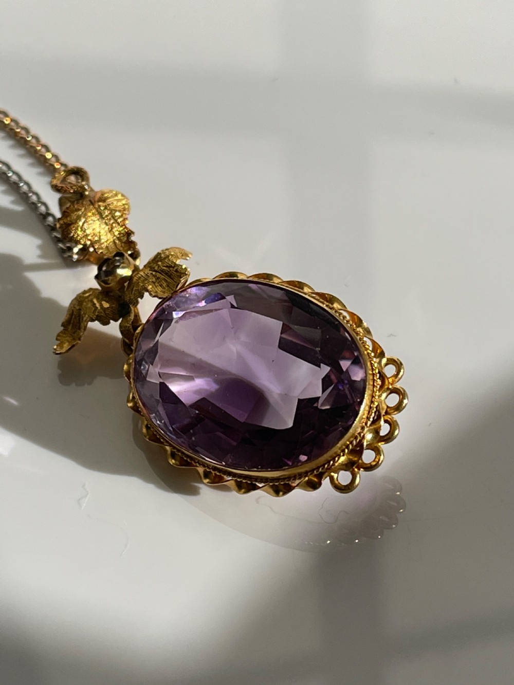 An oval purple faceted amethyst pendant with an ornate foliate gold bail on a delicate chain. View IV