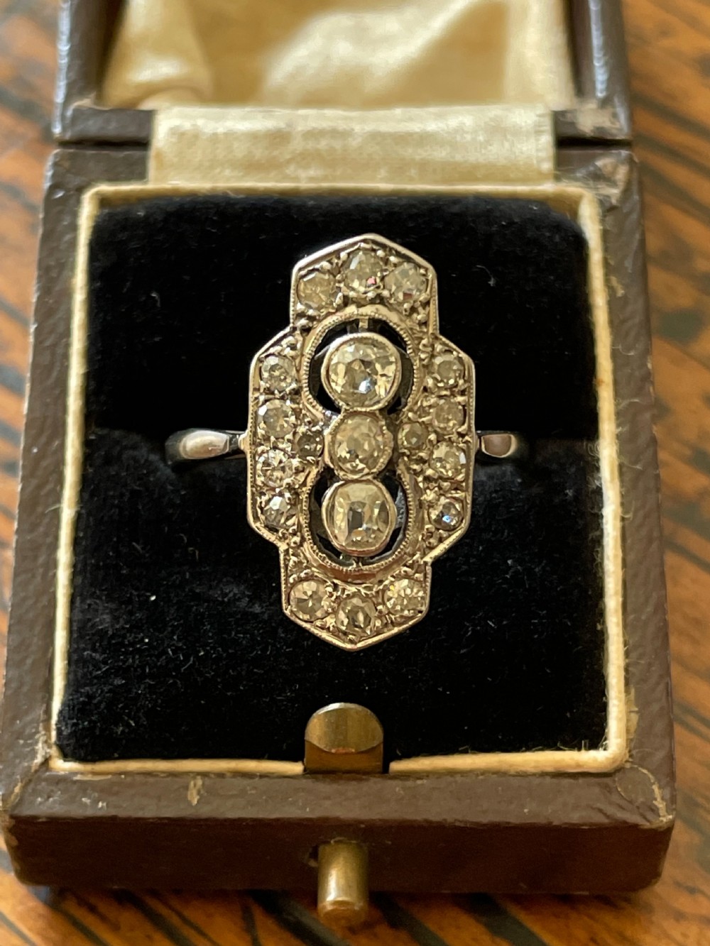 An Edwardian platinum and diamond panel ring featuring three central round diamonds within an elongated geometric frame. View X